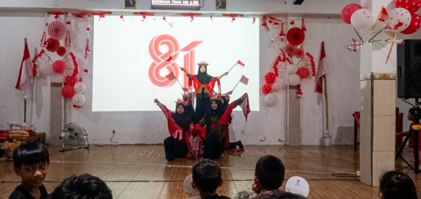Group of young girls in red and black outfits performing a coordinated dance on a stage, with red-and-white decorations and balloons in the background.