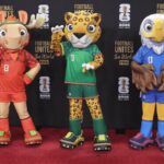 Three colorful sports mascots posing on a red carpet in front of a black backdrop with 'Football Unites the World' branding.