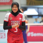 Female volleyball player wearing a red jersey and hijab, number 5, smiling on the court.