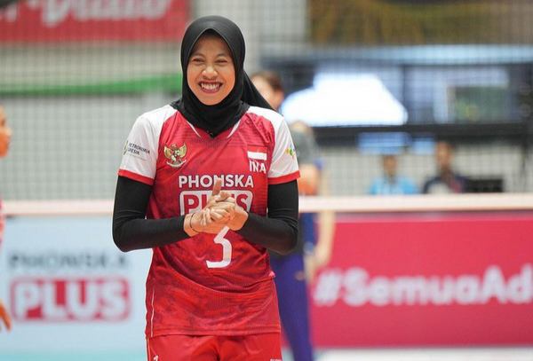 Female volleyball player wearing a red jersey and hijab, number 5, smiling on the court.