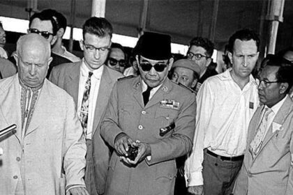 Group of men in suits and a uniformed officer with sunglasses examining a large technical model or control panel at an exhibition, focused on the central display.