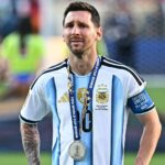 Soccer player in Argentina jersey with a World Cup 2026 medal around his neck on the field.
