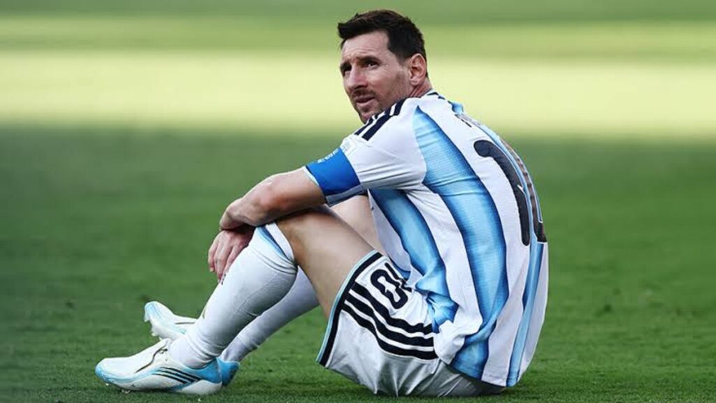 messi laying down by Getty Images - Mabur.co Soccer player sitting on the grass, wearing a light blue and white striped jersey, arms around his knees, looking off to the side.