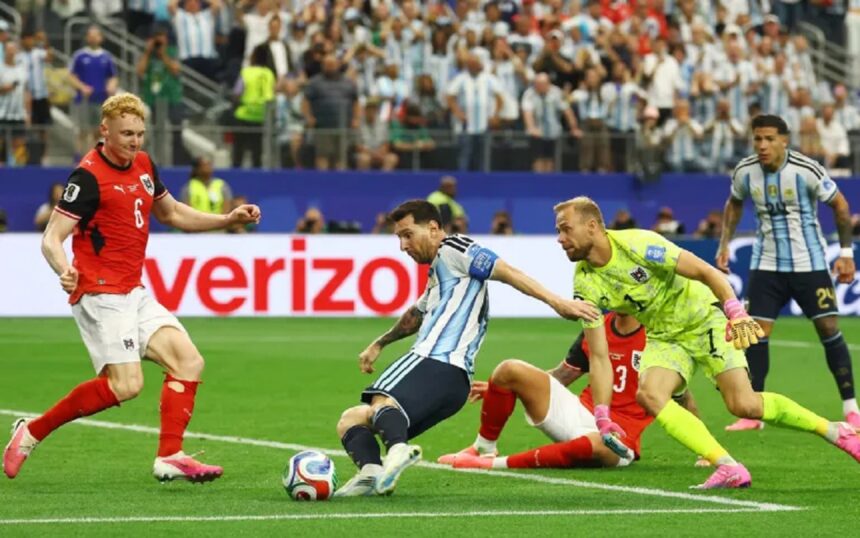 messi vs Austria by al jazeera - Mabur.co Soccer match action: players contest the ball near the goal line as a neon-yellow goalkeeper lunges to reach it. Crowd in the stands watches.