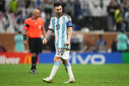 Soccer player wearing Argentina's blue-and-white striped kit with number 10 and a captain's armband, walking on a grass pitch.