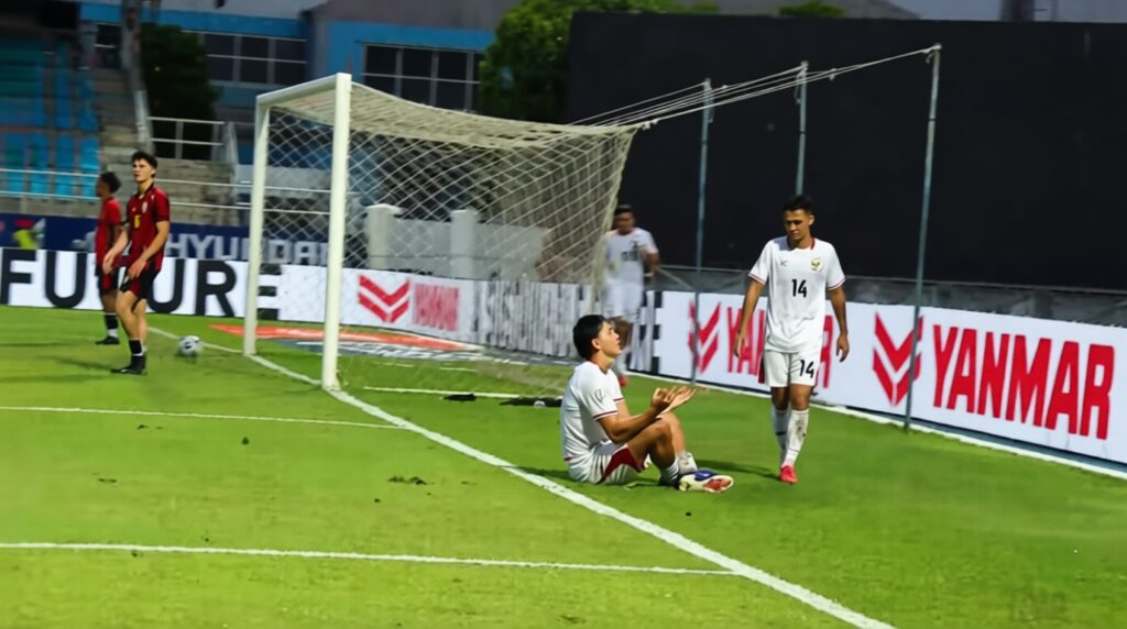 mitchell baker selebrasi haaland by timnas Indonesia OFC FIXX - Mabur.co Soccer scene: a white-team player sits on the grass near the goal with a ball while a teammate in white stands nearby; two red-team players are in the background near the left.