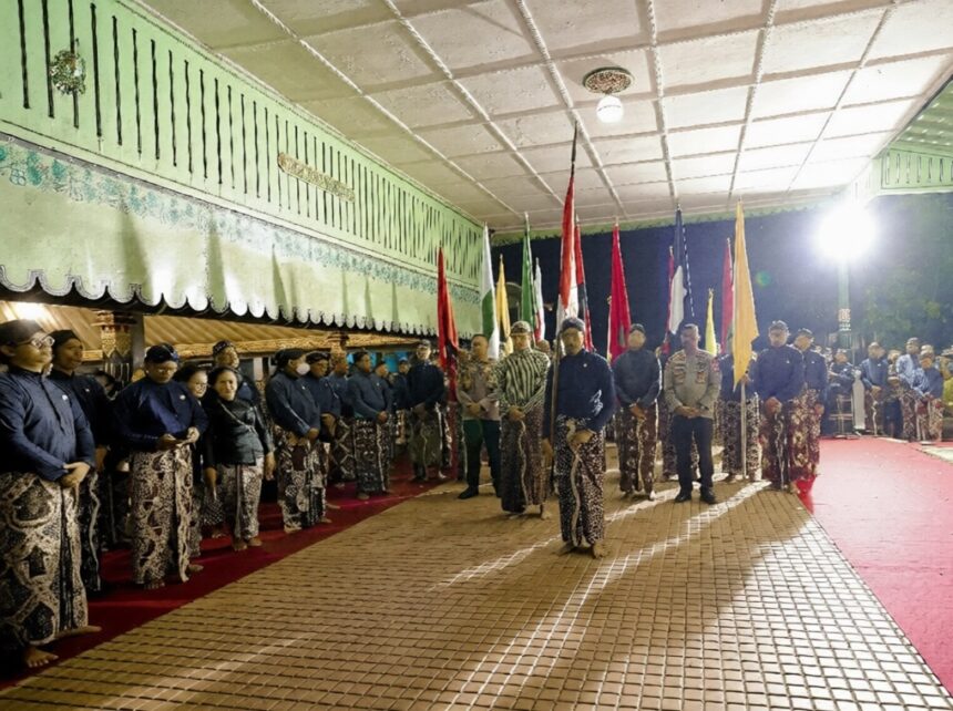 mubeng beteng jogjaprov go id-ezremove FIXX - Mabur.co Group of people in batik attire standing in a line with colorful flags during a night ceremony under a green awning.