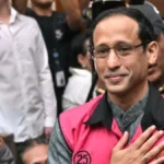 Man in a pink vest with the number 25, hand on chest, amid a crowd of people taking photos behind him.