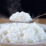 Steaming white rice being scooped from a plate with a spoon