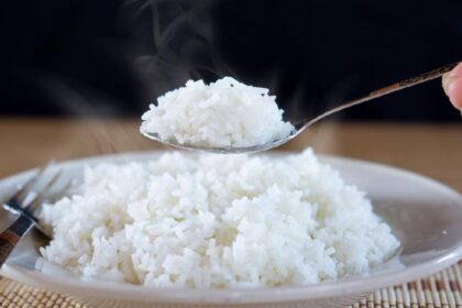 Steaming white rice being scooped from a plate with a spoon