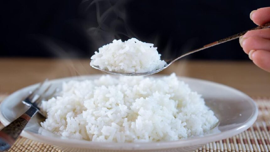 Steaming white rice being scooped from a plate with a spoon