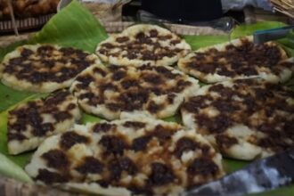 Flatbreads topped with dark, seasoned meat arranged on banana leaves at a market stall
