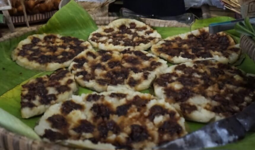 Flatbreads topped with dark, seasoned meat arranged on banana leaves at a market stall