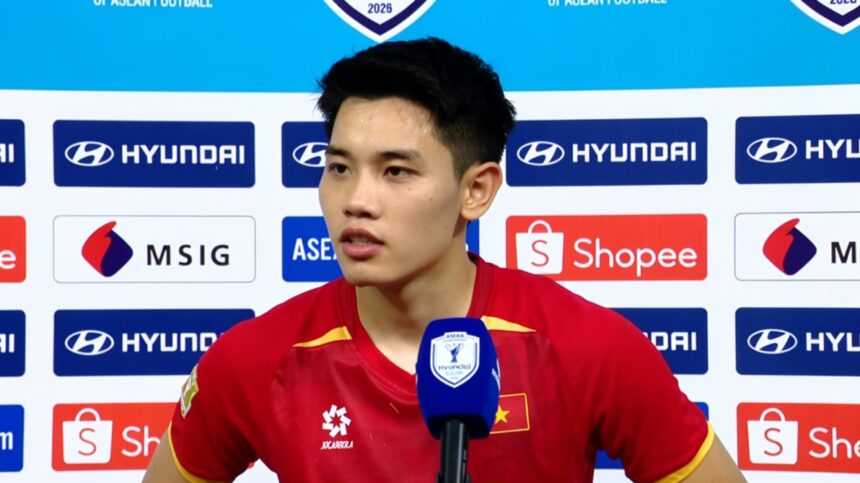 Young Asian football player in a red jersey giving a post-match interview in front of a sponsor backdrop.