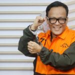 Smiling man in orange inmate uniform displaying handcuffs in his raised hand
