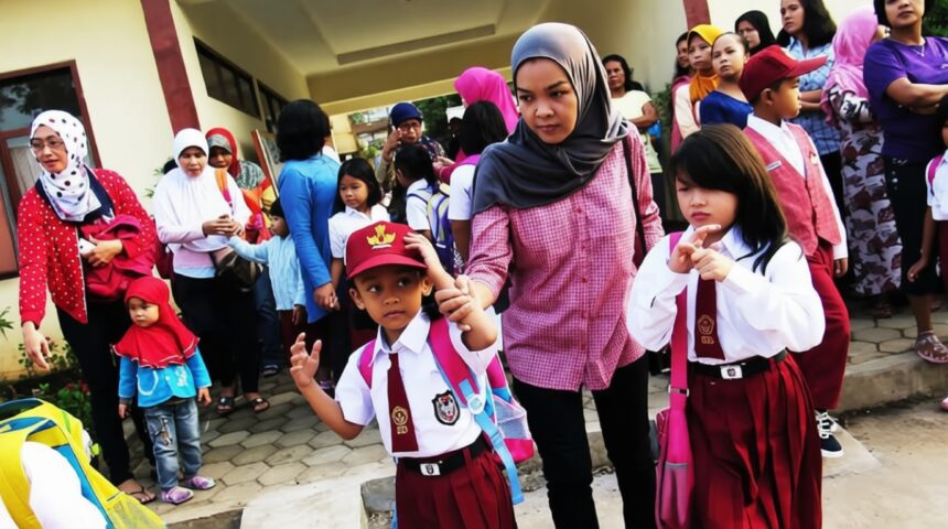 ortu antar anak ke sekolah by Sekretariat Kabinet FIXX - Mabur.co Group of children in uniforms with backpacks outside a school, adults nearby awaiting drop-off.