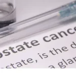 Close-up of a syringe and vial resting on a document that reads 'Prostate cancer'—suggesting medical research or treatment context.