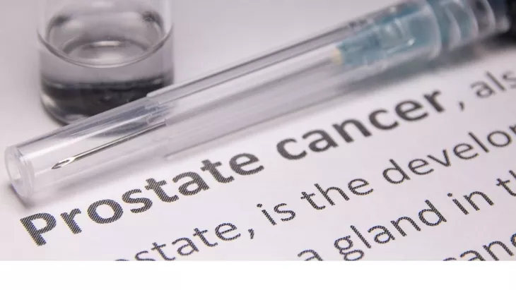 Close-up of a syringe and vial resting on a document that reads 'Prostate cancer'—suggesting medical research or treatment context.