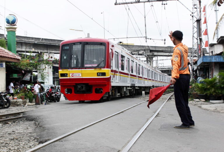 Train paused on tracks as a uniformed railway worker signals with a red flag beside the rails.
