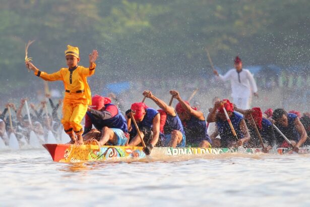 Dragon boat race: a yellow-clad paddler stands at the prow with arms raised, leading a team of paddlers through splashing water.