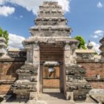 Stone temple gate with layered pagoda-style towers, brick walls, and a clear blue sky behind.