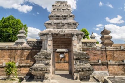 Stone temple gate with layered pagoda-style towers, brick walls, and a clear blue sky behind.