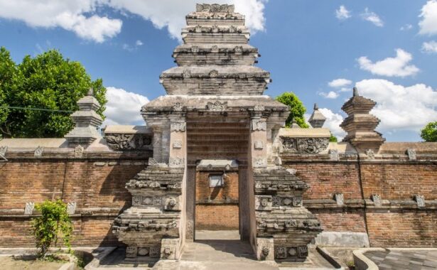 Stone temple gate with layered pagoda-style towers, brick walls, and a clear blue sky behind.