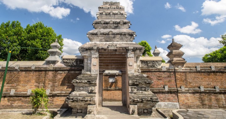 Stone temple gate with layered pagoda-style towers, brick walls, and a clear blue sky behind.