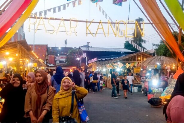 People posing under a colorful festival entrance that reads PASAR KANGEN at a busy night market.