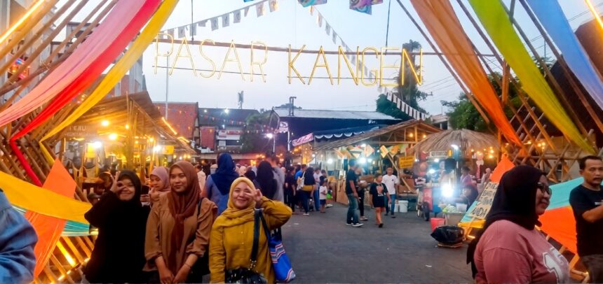 People posing under a colorful festival entrance that reads PASAR KANGEN at a busy night market.
