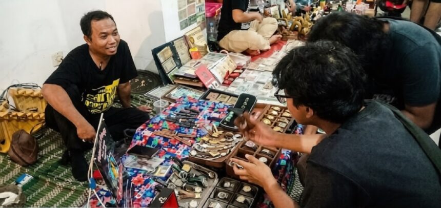 Vendor sits on the floor beside a colorful display of watches, smiling at a customer inspecting timepieces on a market stall table.