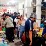 Crowded indoor book market with tables full of stacked books and shoppers browsing under colorful bunting ground overhead.