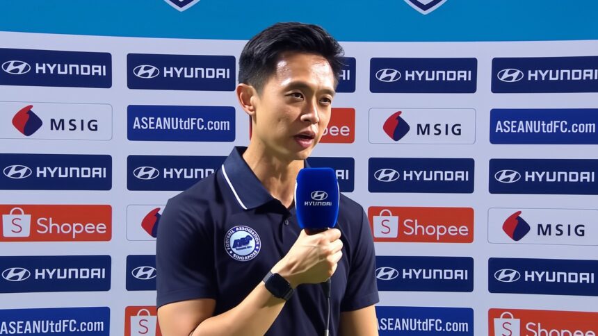 A man interviewed on a sports backdrop holding a blue Hyundai microphone, wearing a navy polo shirt with a badge.