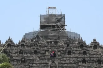 Stone temple wall with multiple niches and a central arched opening, covered in scaffolding for renovation on the upper levels.