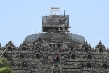 Stone temple wall with multiple niches and a central arched opening, covered in scaffolding for renovation on the upper levels.