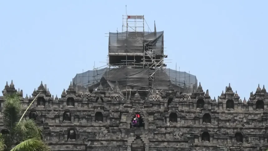 Stone temple wall with multiple niches and a central arched opening, covered in scaffolding for renovation on the upper levels.