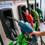Person refueling a vehicle with a blue gasoline nozzle at a pump; several colored nozzles are visible in the background.
