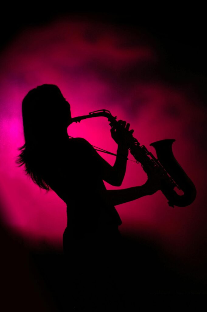 Silhouette of a saxophonist playing on stage with pink fog behind them.