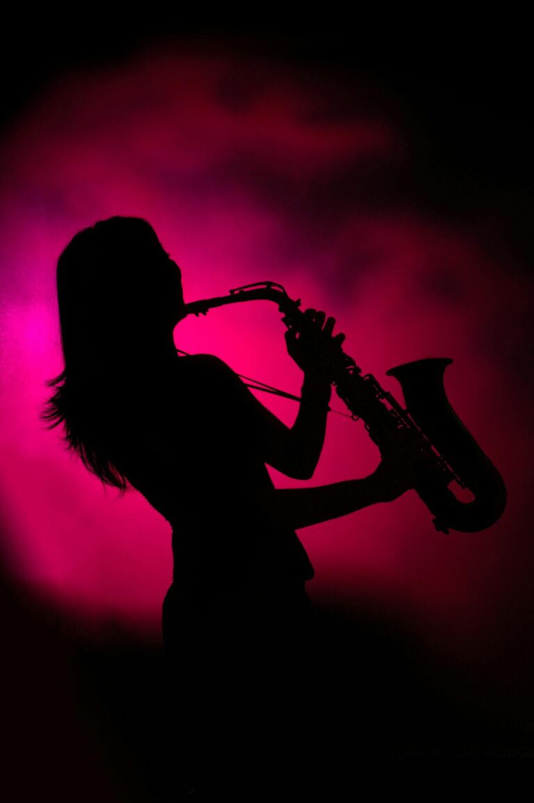 Silhouette of a saxophonist playing on stage with pink fog behind them.