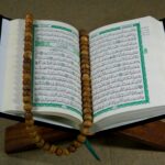 Open Quran resting on a wooden stand with a wooden prayer bead rosary laid across its pages.