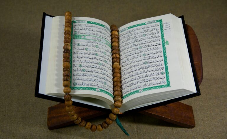 Open Quran resting on a wooden stand with a wooden prayer bead rosary laid across its pages.