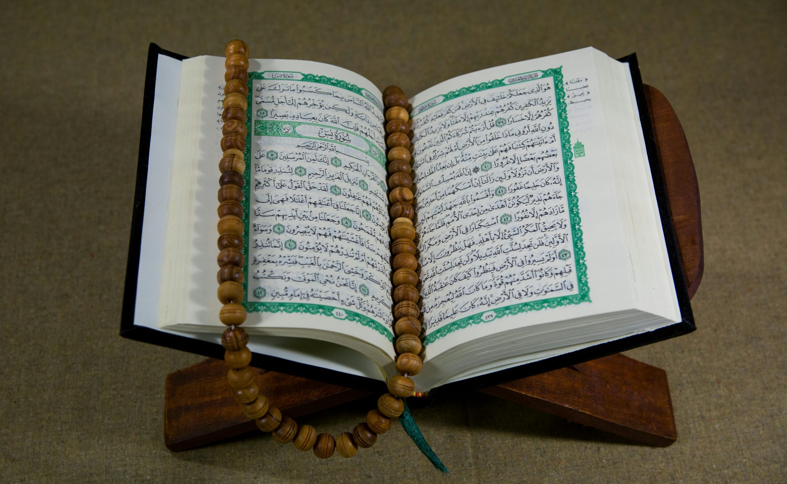 Open Quran resting on a wooden stand with a wooden prayer bead rosary laid across its pages.