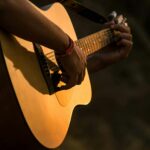 Close-up of a person strumming an acoustic guitar outdoors, with warm sunlight on the wood body.