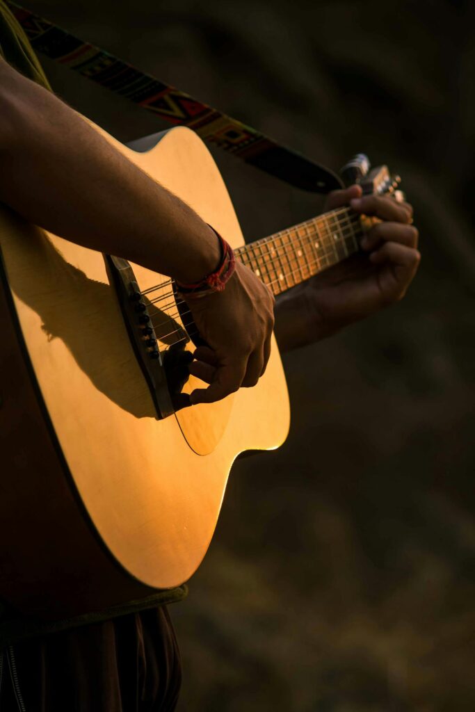 Close-up of a person strumming an acoustic guitar outdoors, with warm sunlight on the wood body.