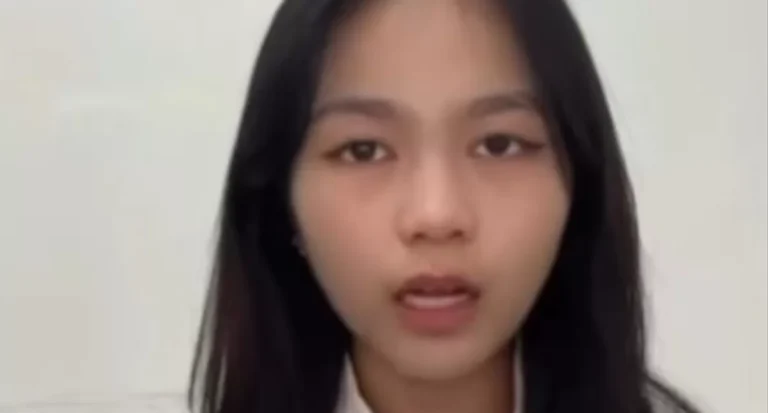 Young woman speaks directly to the camera against a light background, likely recording a video message or vlog.
