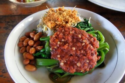Plate of sautéed greens with a chunky peanut sauce topping, roasted peanuts, and crispy fried onions on the side.