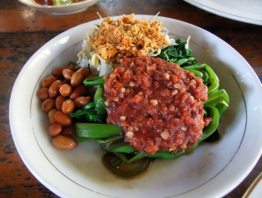 Plate of sautéed greens with a chunky peanut sauce topping, roasted peanuts, and crispy fried onions on the side.