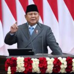 Indonesian official giving a speech at a podium decorated with red and white roses, national flags in the background.
