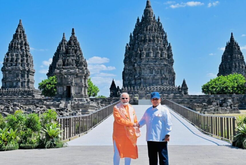 presidenrigoid-08072026171437-6a4e230d4c56e633336593-e1783505709553-1280x721 - Mabur.co Two men in bright robes shake hands on a sunny walkway in front of tall ancient Hindu temple towers.
