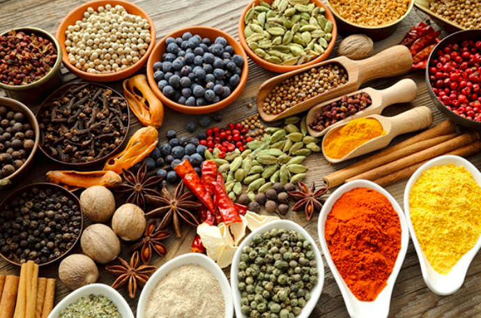 Assorted spices and spice blends arranged in bowls and scoops on a wooden table.